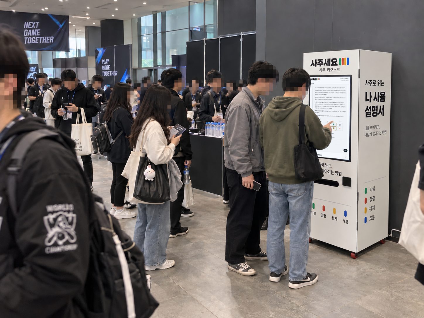 게임 행사 로비에서 관람객들이 사주 자판기 화면을 보는 장면
