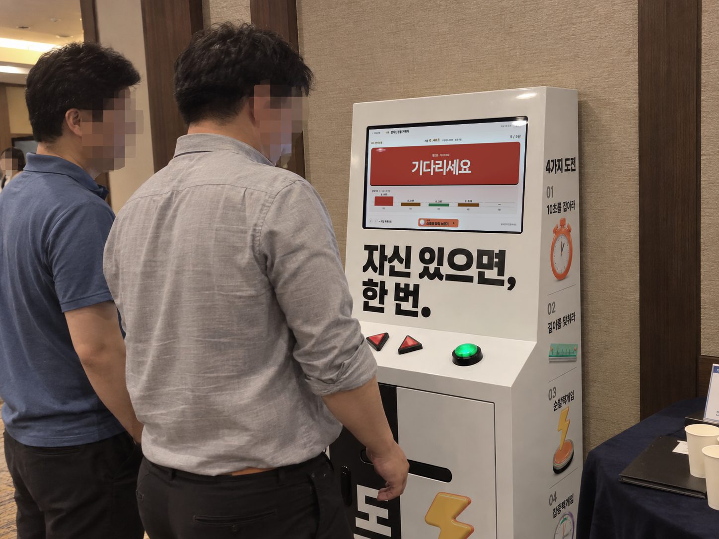실내 로비에서 두 참가자가 감각게임 키오스크의 반사신경 게임 신호를 기다리는 장면